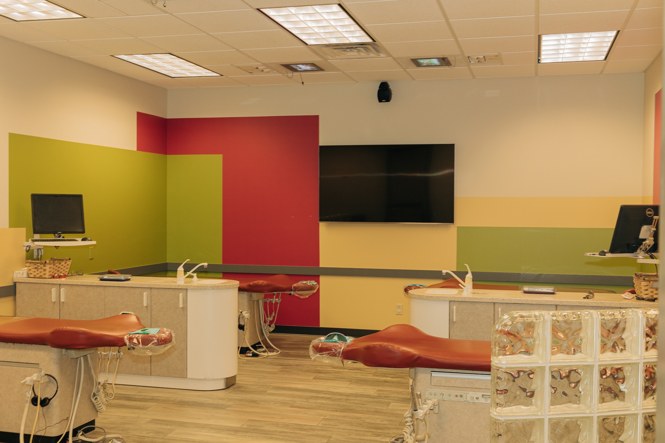 A modern dental office with colorful walls, dental chairs, computer monitors, and clean, organized spaces. No people or recognizable landmarks present.