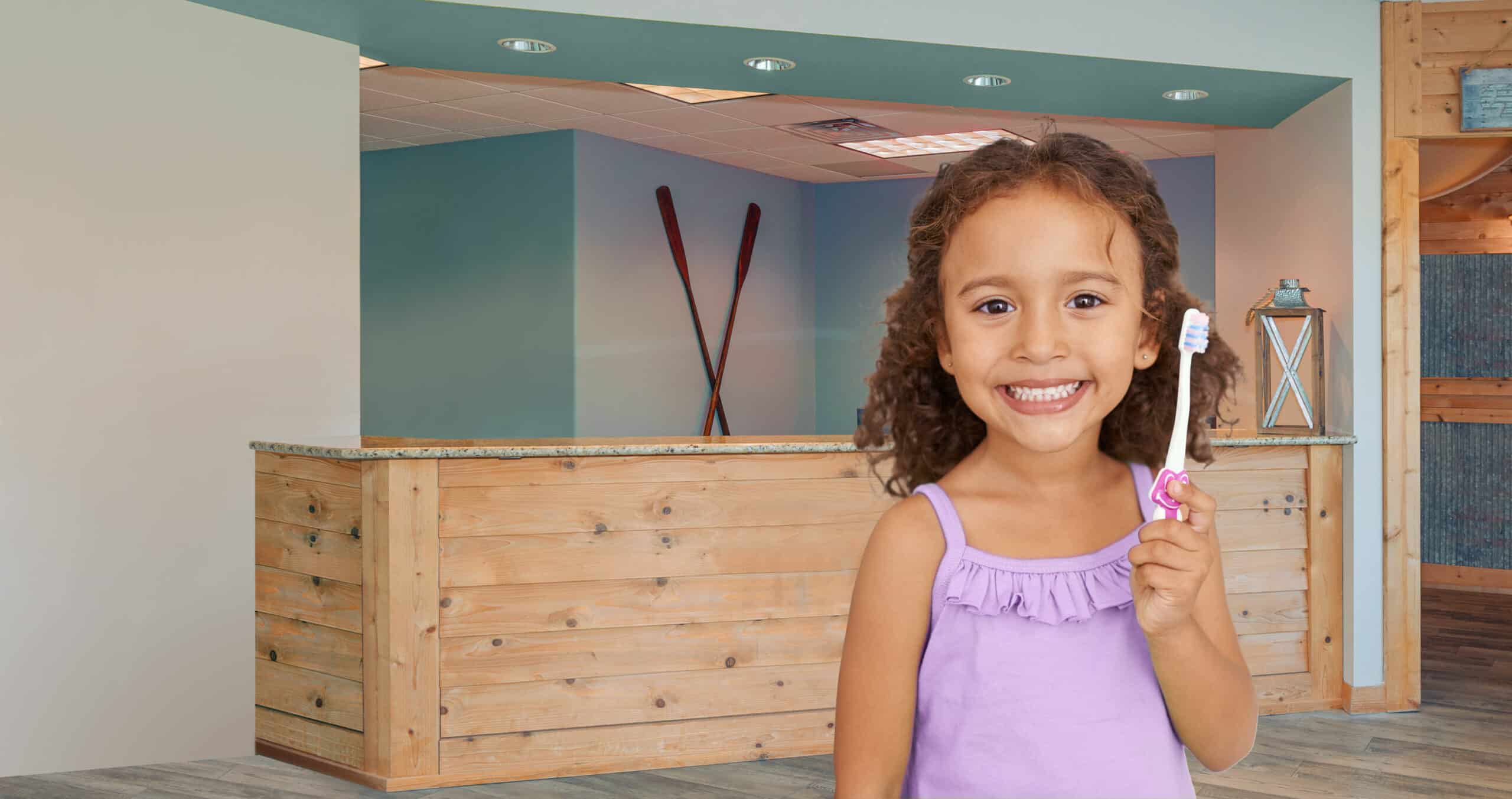 A child smiles holding a toothbrush in a rustic reception area with wooden decor and ski-themed wall art in the background.